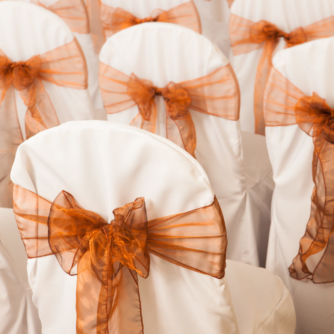 White wedding bouquet in the background with chairs in foreground arranged in rows and dressed with ribbons