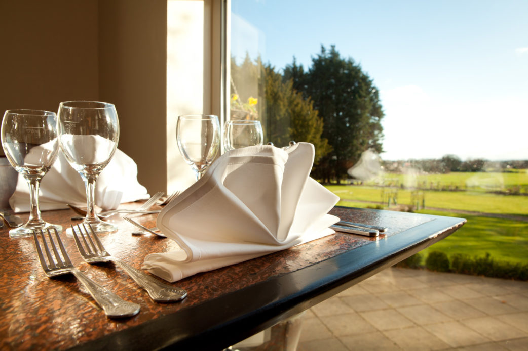 Restaurant table, close up of folded napkin, blurred view of garden out of the window