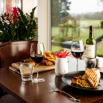 Restaurant table, steak and chips, chicken breast, red wine, blurred view of garden out of the window