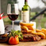 Restaurant table, close up of steak and chips, red wine, blurred view of garden out of the window