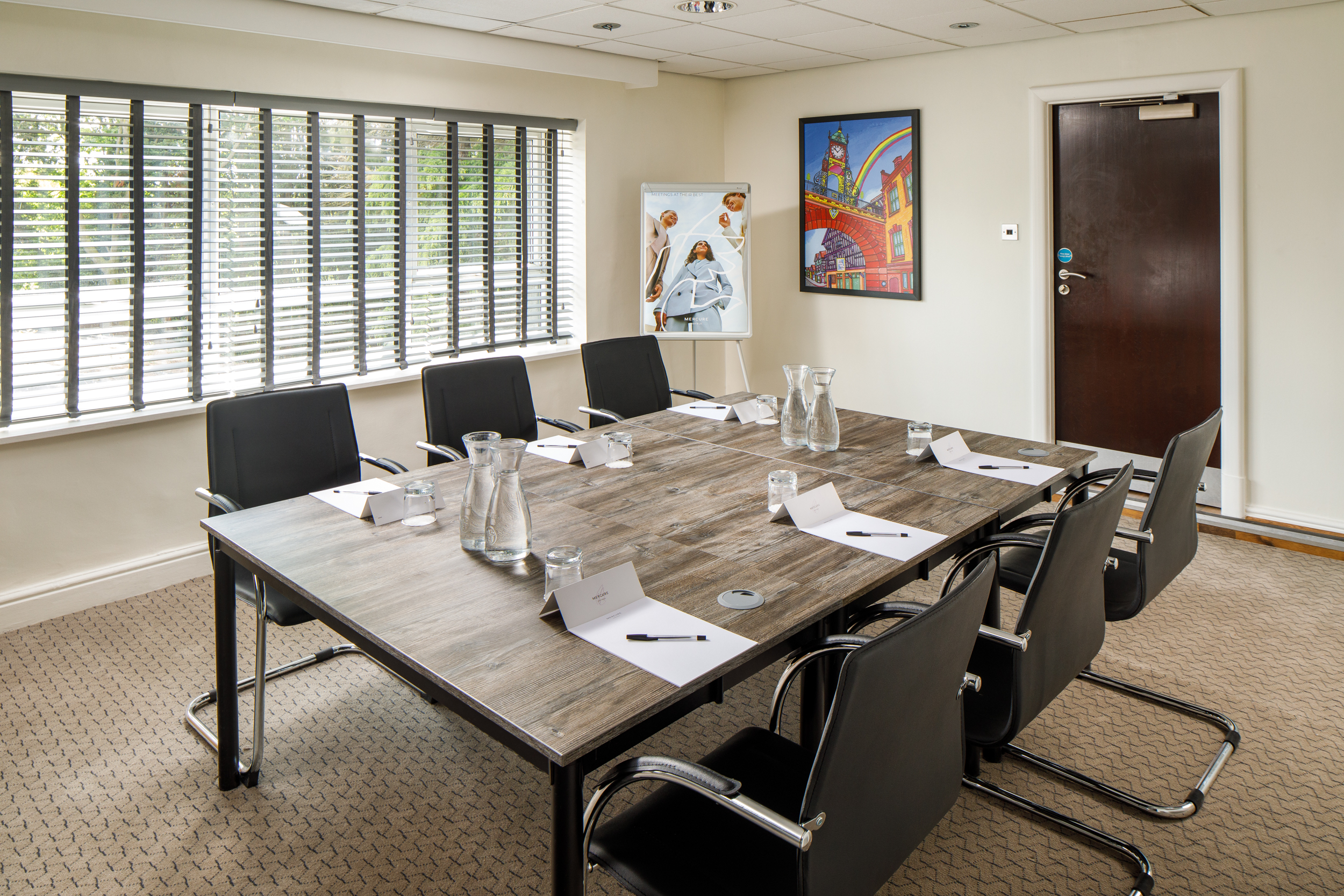 Meeting table at Mercure London Watford, black leather office chairs around a wooden table with glasses of water and apples