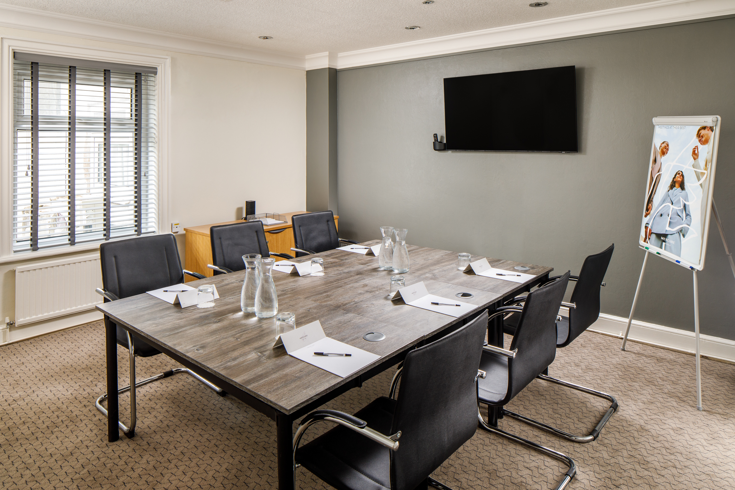 Syndicate 1 (3) Meeting table at Mercure London Watford, black leather office chairs around a wooden table with glasses of water and apples